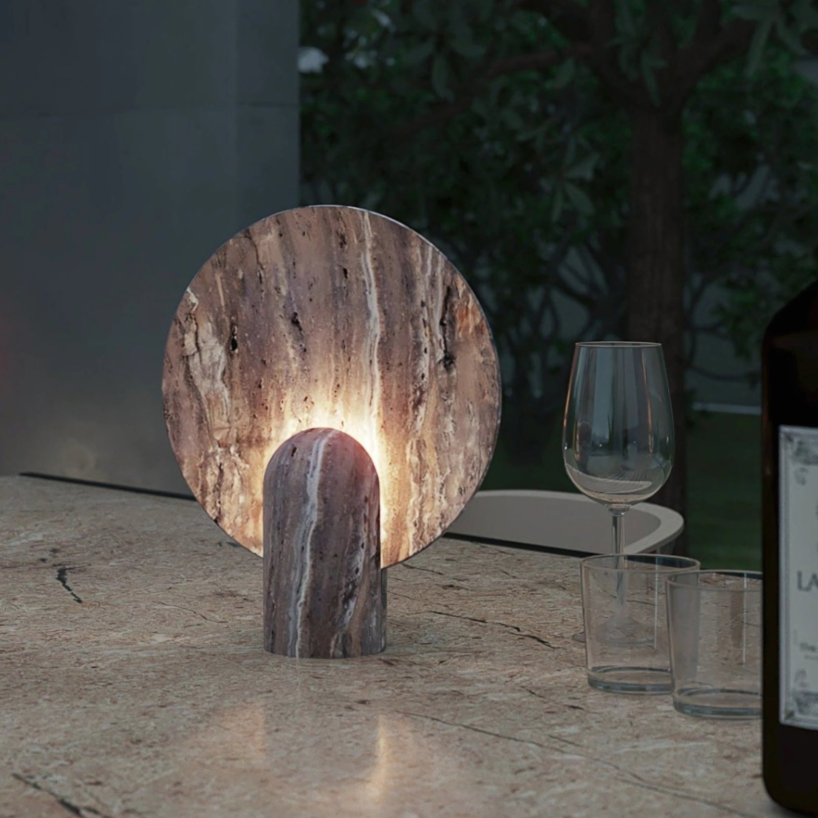Fosse travertine table lamp from Love Hohm on a stone surface with glasses and a bottle in the background