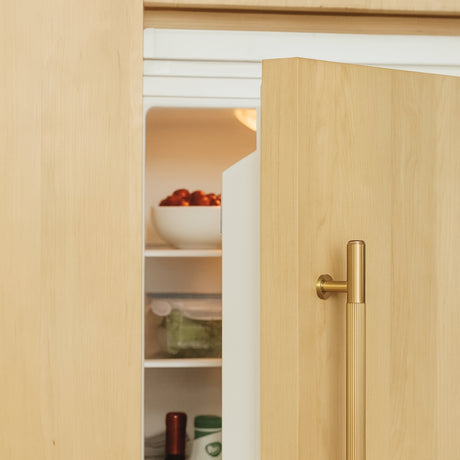 Hone brass pull on a panel appliance refrigerator in light wood color.