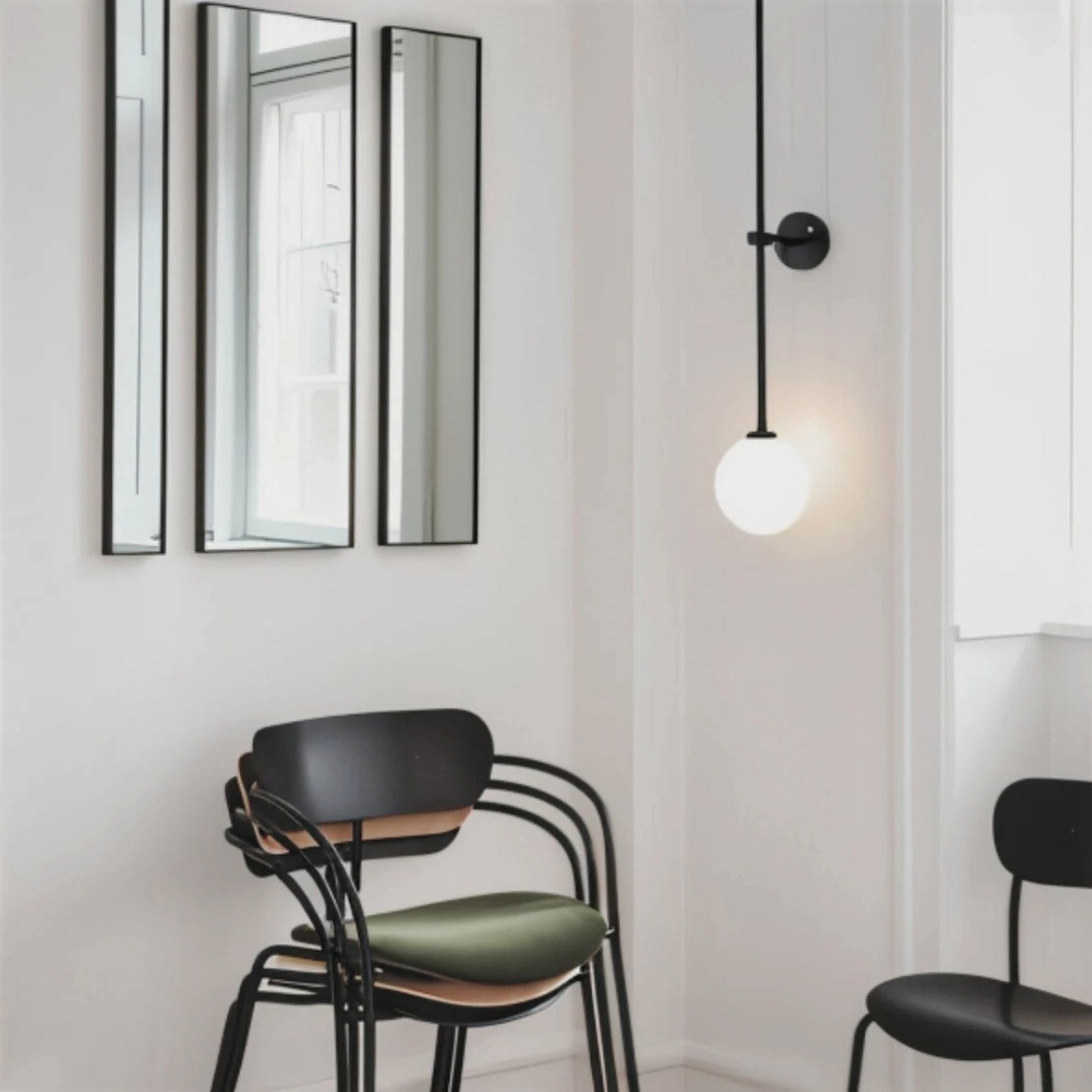 Modern interior with black chairs, a Segment wall light from Love Hohm, and mirrors on a white wall.