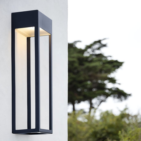 Threshold outdoor wall light from Love Hohm on a white wall with blurred greenery in the background