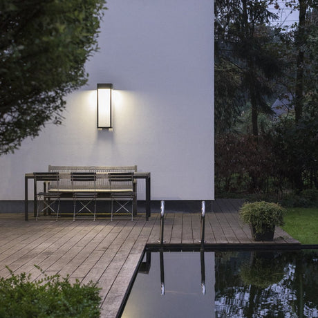 Outdoor setting with a bench, Threshold outdoor wall lamp from Love Hohm, and pool at night.
