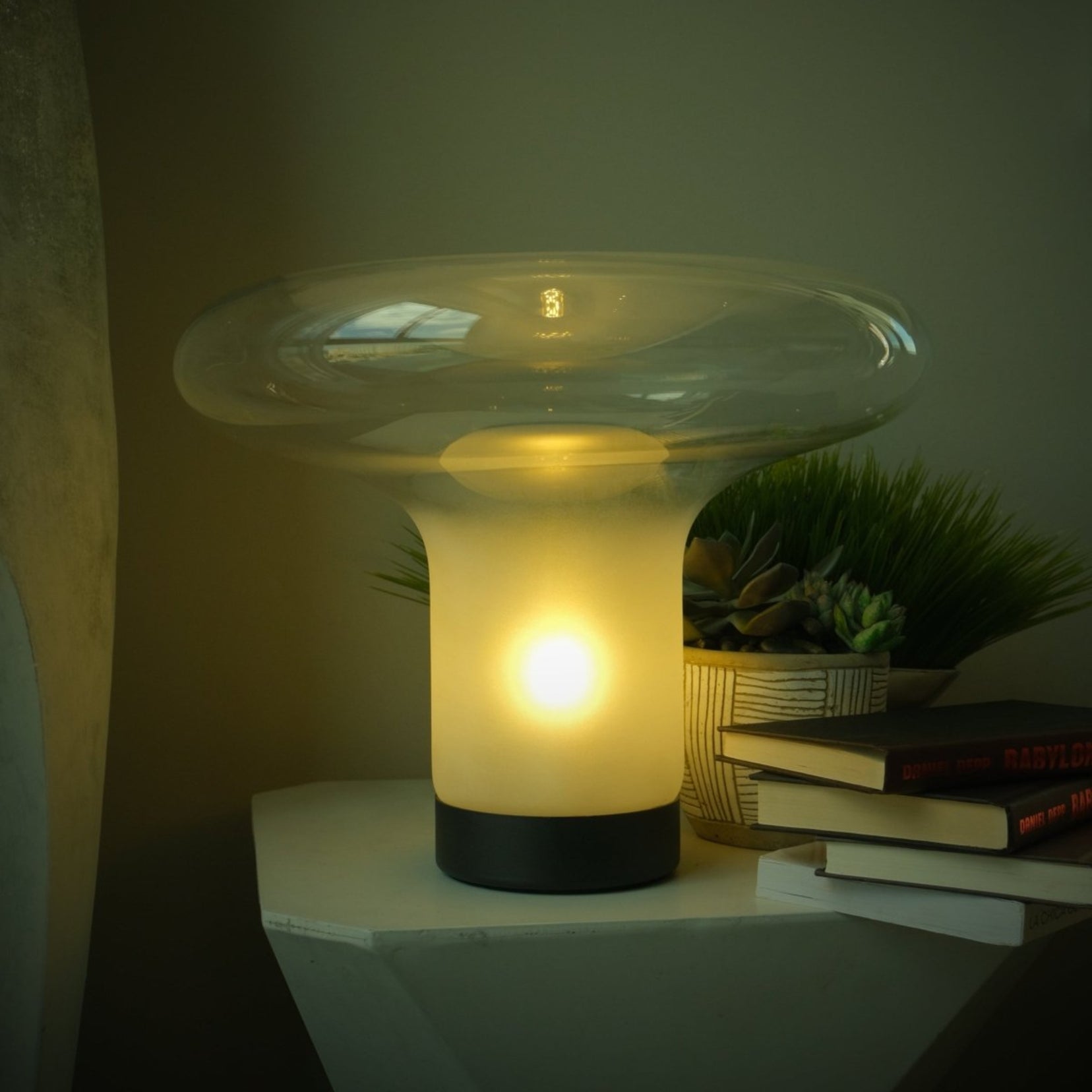 Vault table lamp from Love Hohm with a unique design on a surface with books and plants in the background