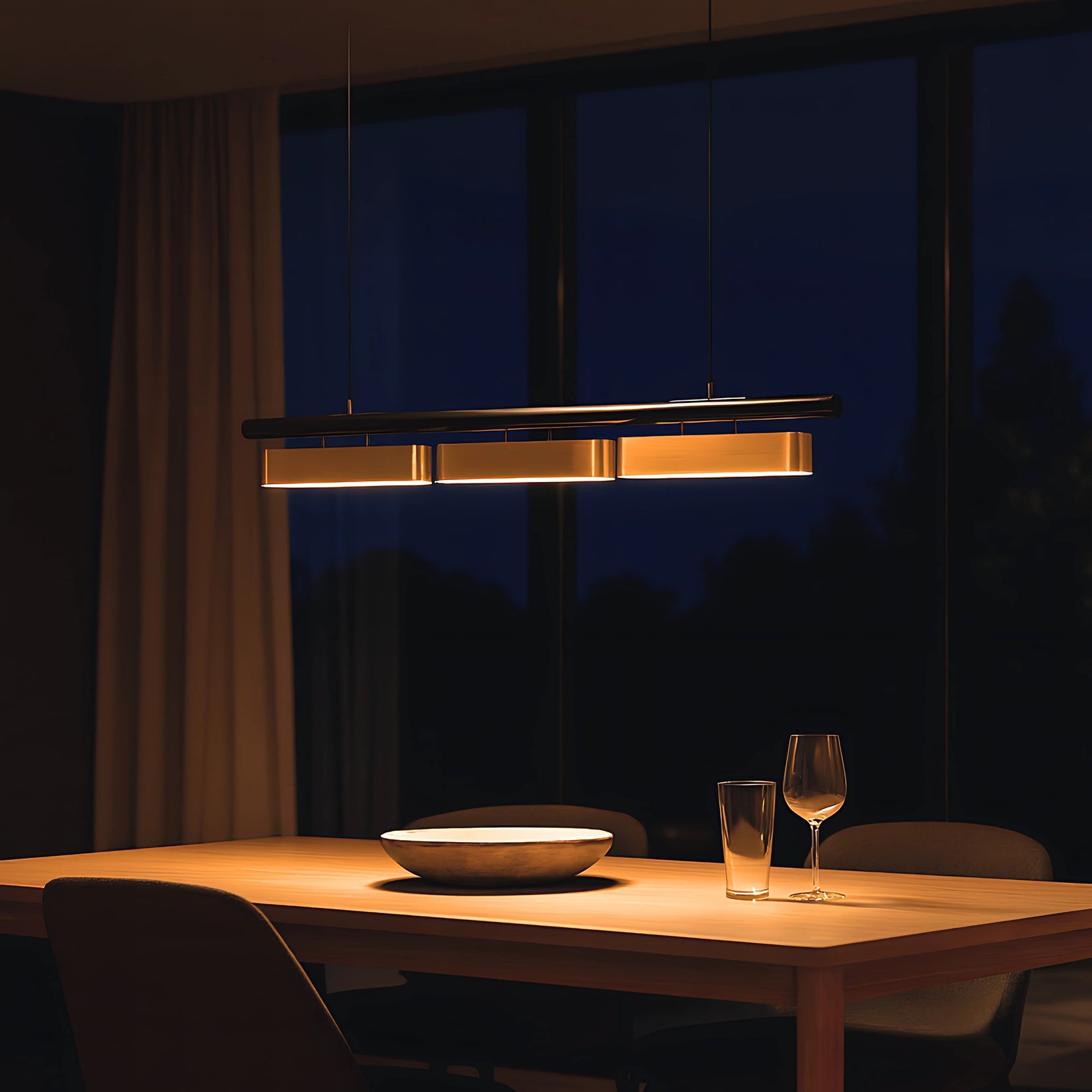Dining table with a bowl and glasses under a Vector Chandelier from Love Hohm in a dimly lit room.