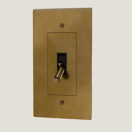 Verge brass toggle from Love Hohm with a black toggle switch on a beige background