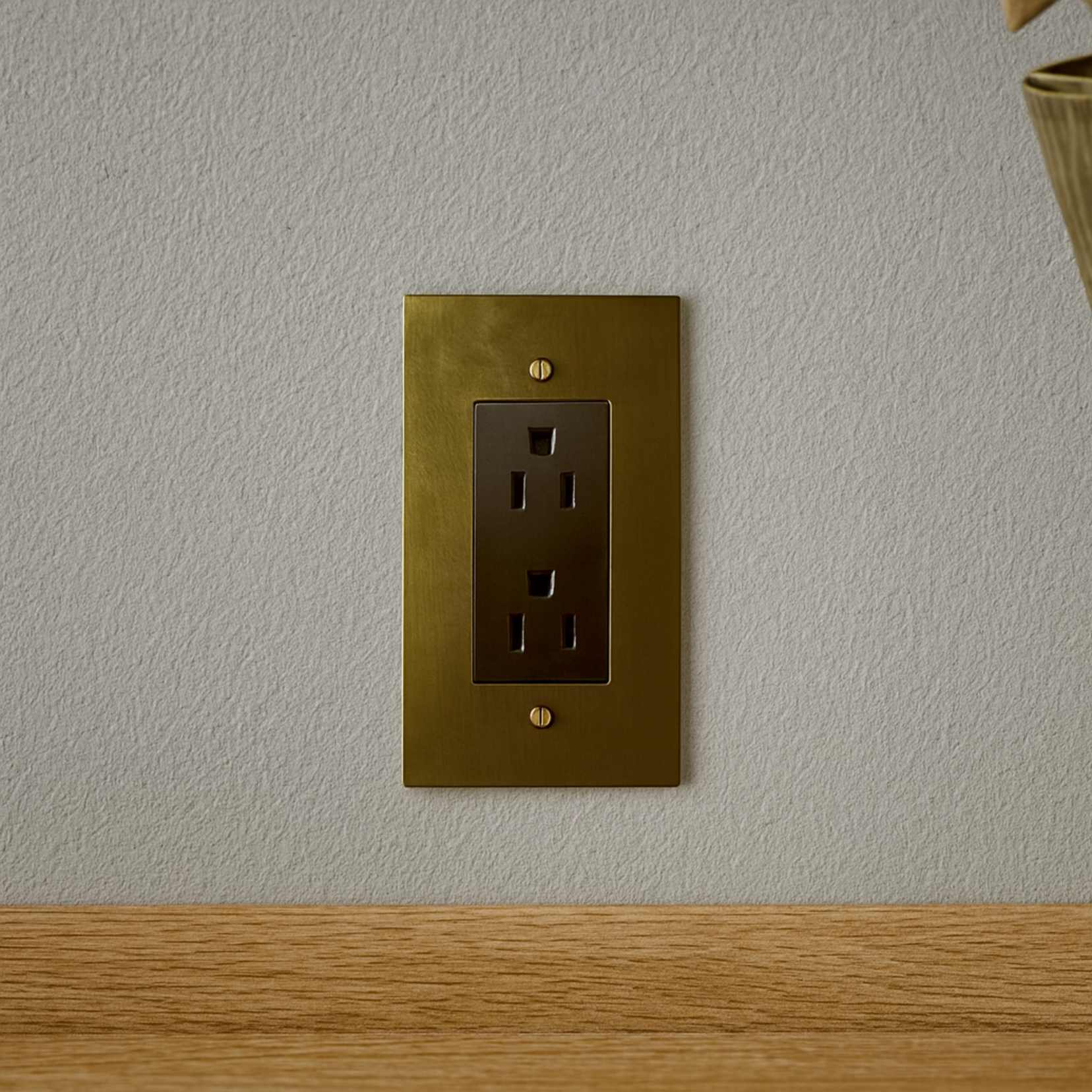 Verge brass outlet from Love Hohm on a light gray wall with a wooden surface at the bottom.