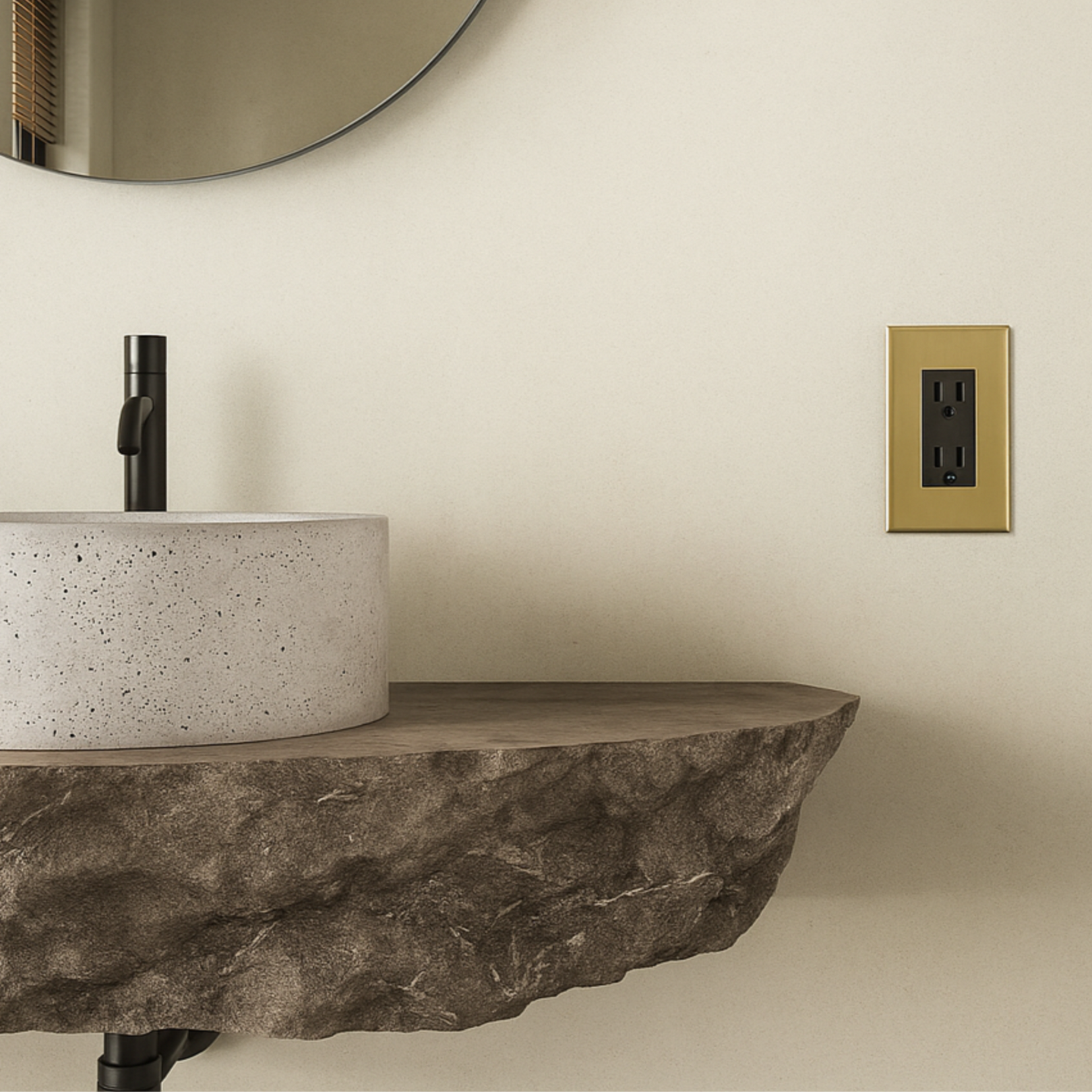 Bathroom vanity with stone countertop, round mirror, and Verge brass outlet from Love Hohm.